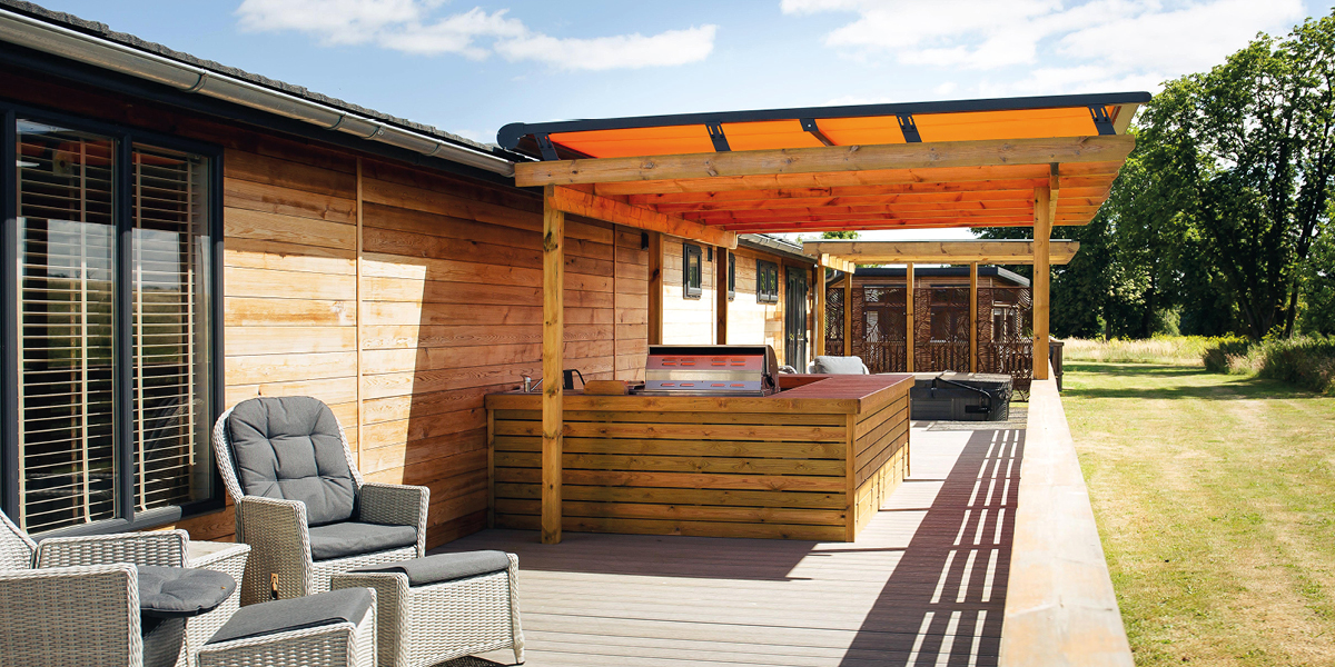 A roof blind attached to an existing wooden pergola, covering a BBQ area.