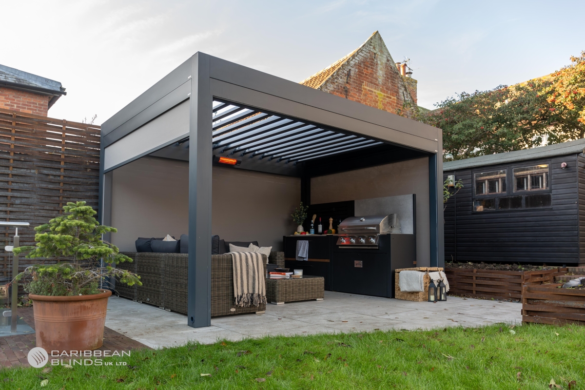 Grillo louvred pergola in anthracite grey with open roof louvres, side screens and patio heater over an outdoor kitchen and bar