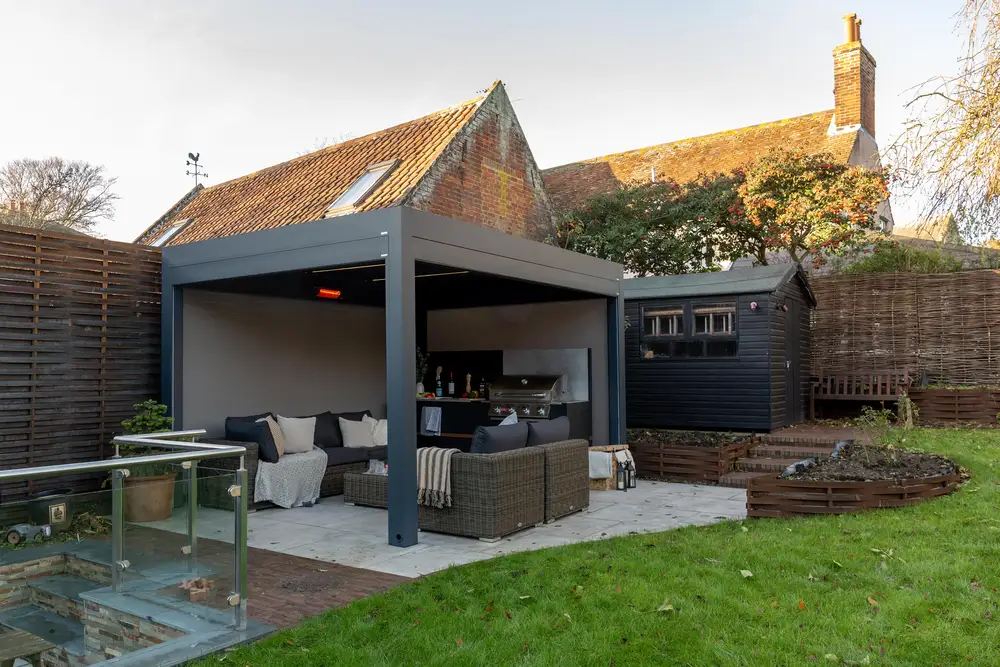 Contemporary garden seating area with a dark grey outdoor living pod, rattan furniture and a built-in barbecue.