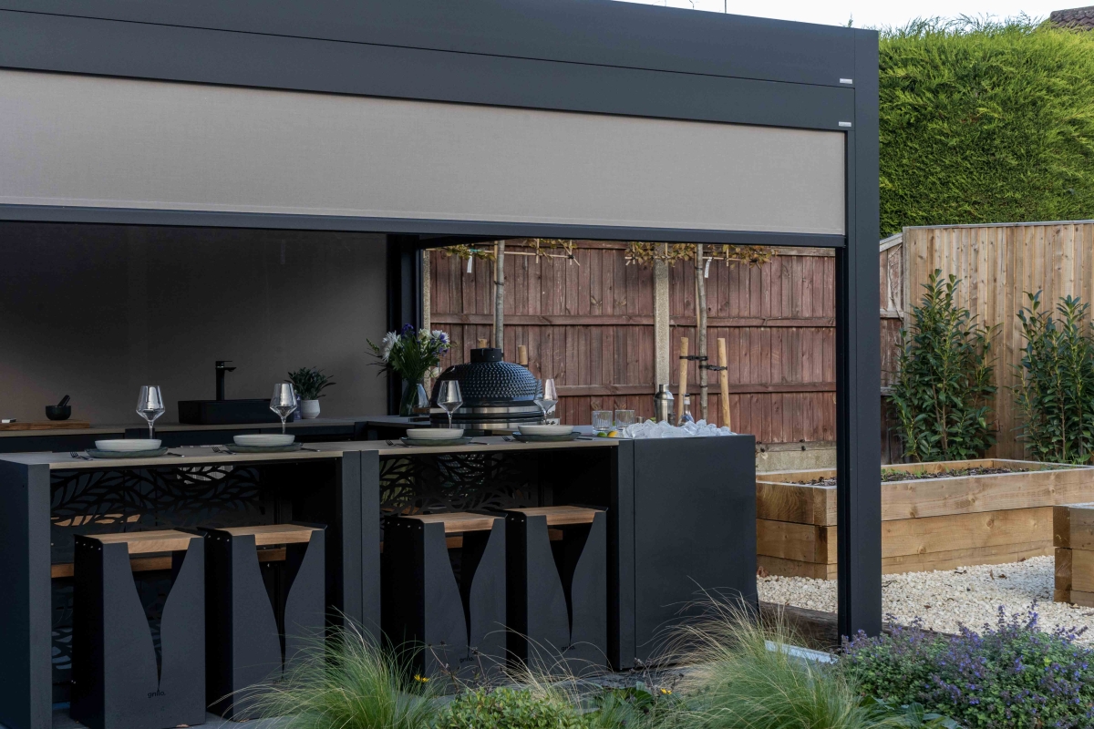 Grillo louvred pergola in anthracite grey with open roof louvres, side screens and patio heater over an outdoor kitchen and bar
